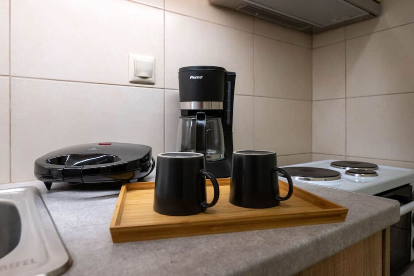 Eine Küche mit Kaffeemaschine, zwei Tassen und einem Waffeleisen auf einer Ablagefläche.