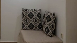 Ein Eckzimmer mit einem beigefarbenen Sofa, gemusterten Kissen und einem gerahmten abstrakten Gemälde an der Wand.