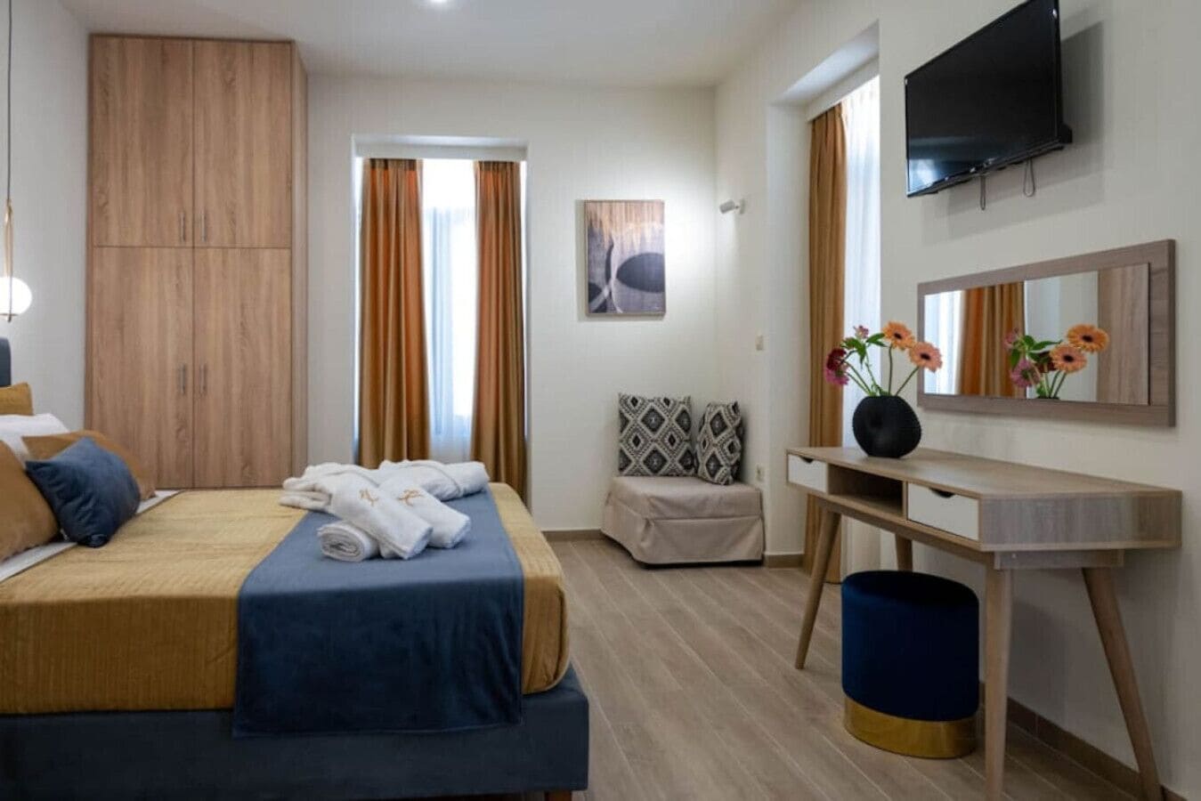 Hotellihuone, jossa on sänky, työpöytä, tuoli, televisio ja ikkuna, jossa on verhot.