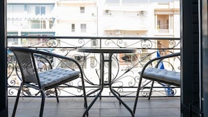 Ein Balkon mit zwei Korbstühlen und einem Tisch, mit Blick auf eine Wohngegend und Gebäude.