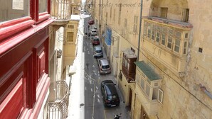 Una calle estrecha con coches aparcados y una moto, bordeada por edificios con balcones y ventanas de arco.