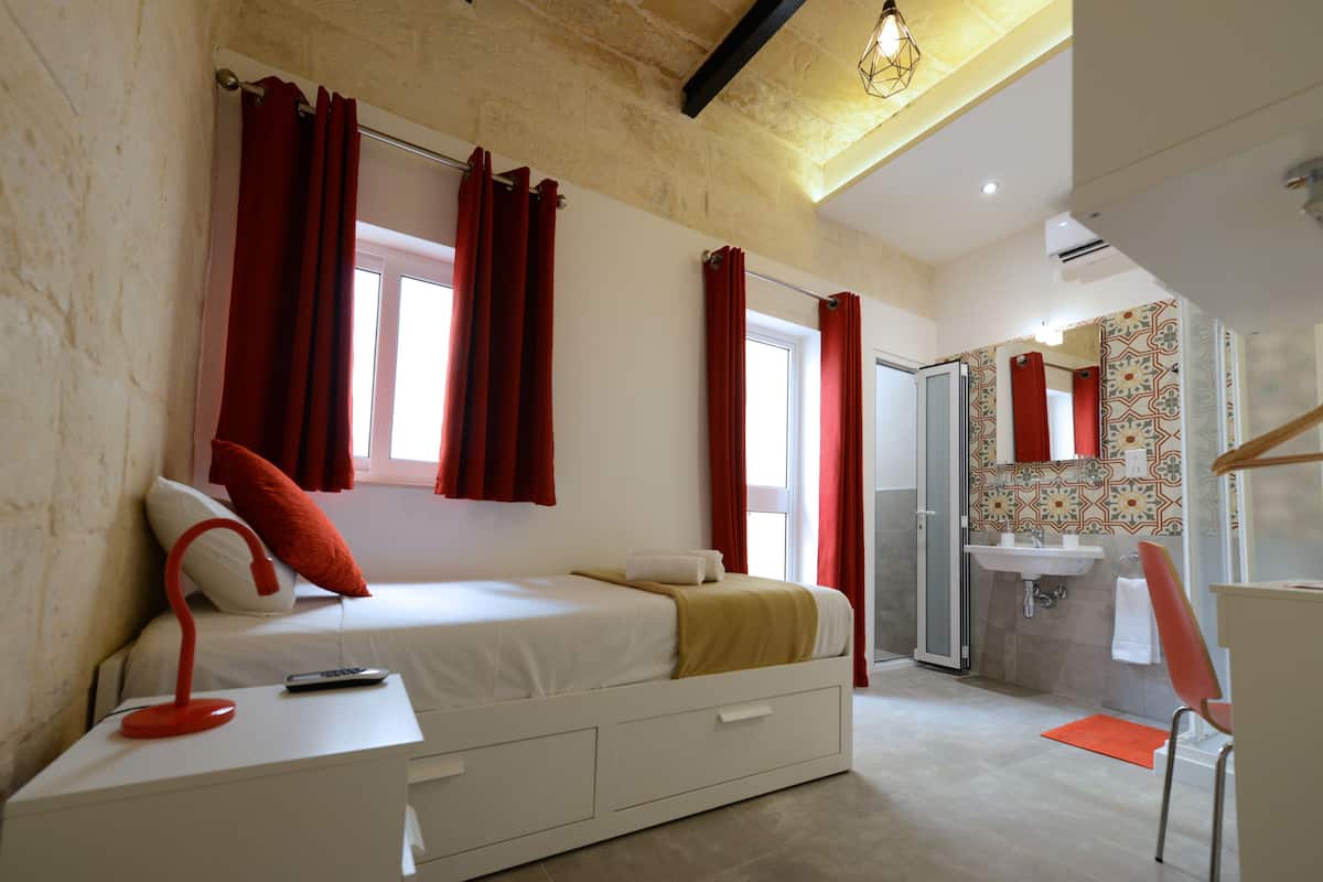 Un dormitorio con cama, mesita de noche y baño con lavamanos y espejo.