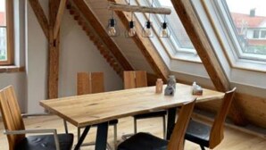 Een eethoek met een houten tafel en stoelen, een schuin dak met zichtbare balken en dakramen.