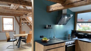 Een moderne keuken met houten balken, een zwart aanrecht en uitzicht op de stad door een groot raam.