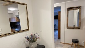 Een hal met een zwarte console tafel, een vaas met bloemen, een grote spiegel en een houten kruk.