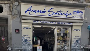 Fachada con un letrero que dice "Armando Scaturcio" y "BAR PASTICCERIA ROSTICCERIA". Hay áreas de estar al aire libre con sillas y mesas de metal.