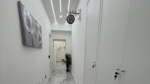 Un pasillo con piso de mármol, un reloj, una puerta y una planta.