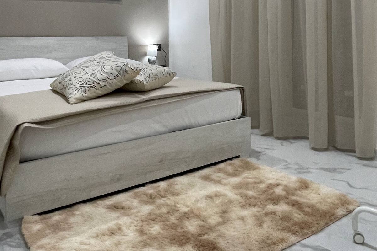 Ein modernes Schlafzimmer mit einem Bett, einem flauschigen Teppich, einem Nachttisch und einer Wandleuchte.