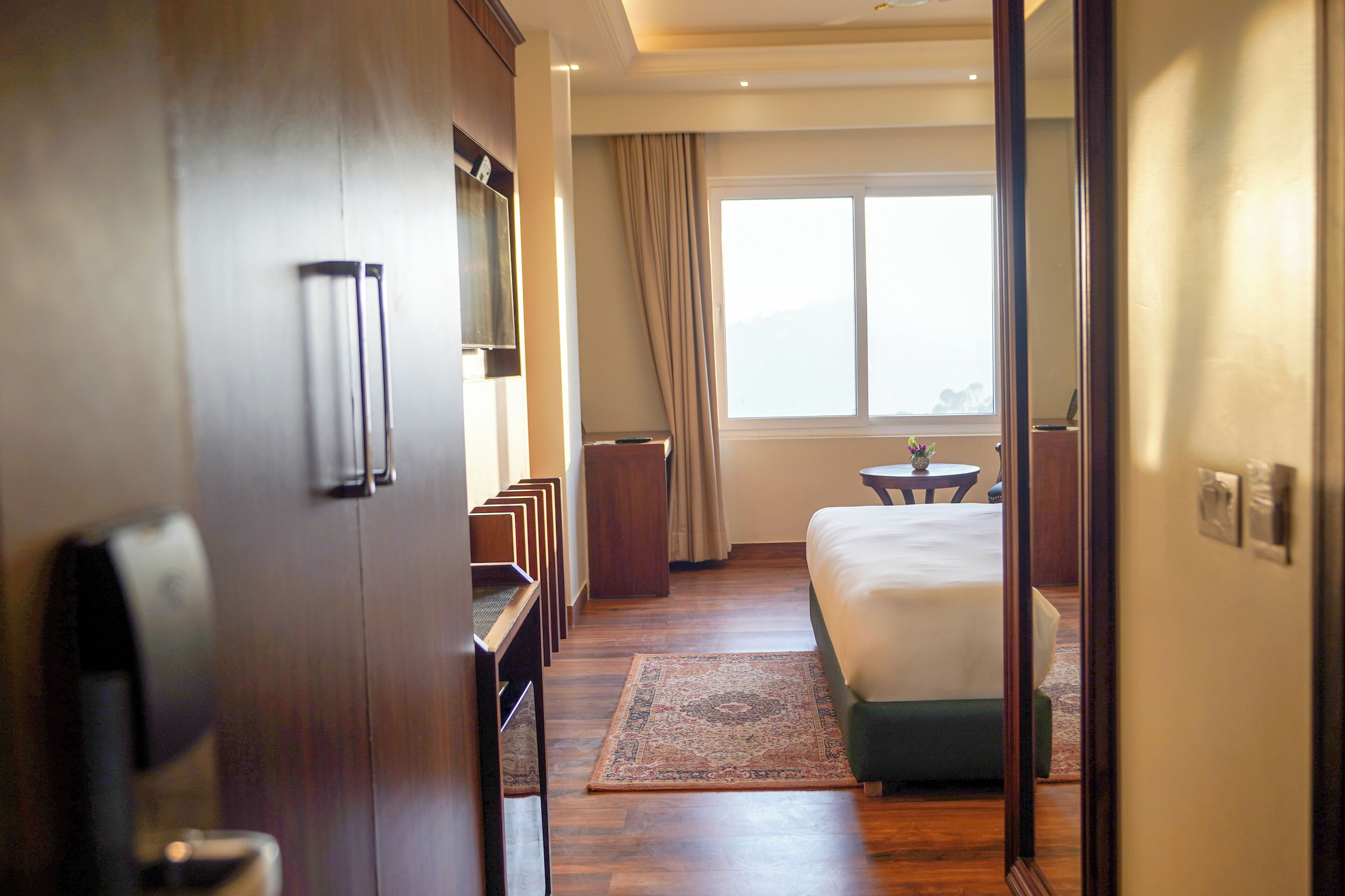 Une chambre d’hôtel avec un lit, un bureau, une chaise, une petite table et une fenêtre avec des rideaux.