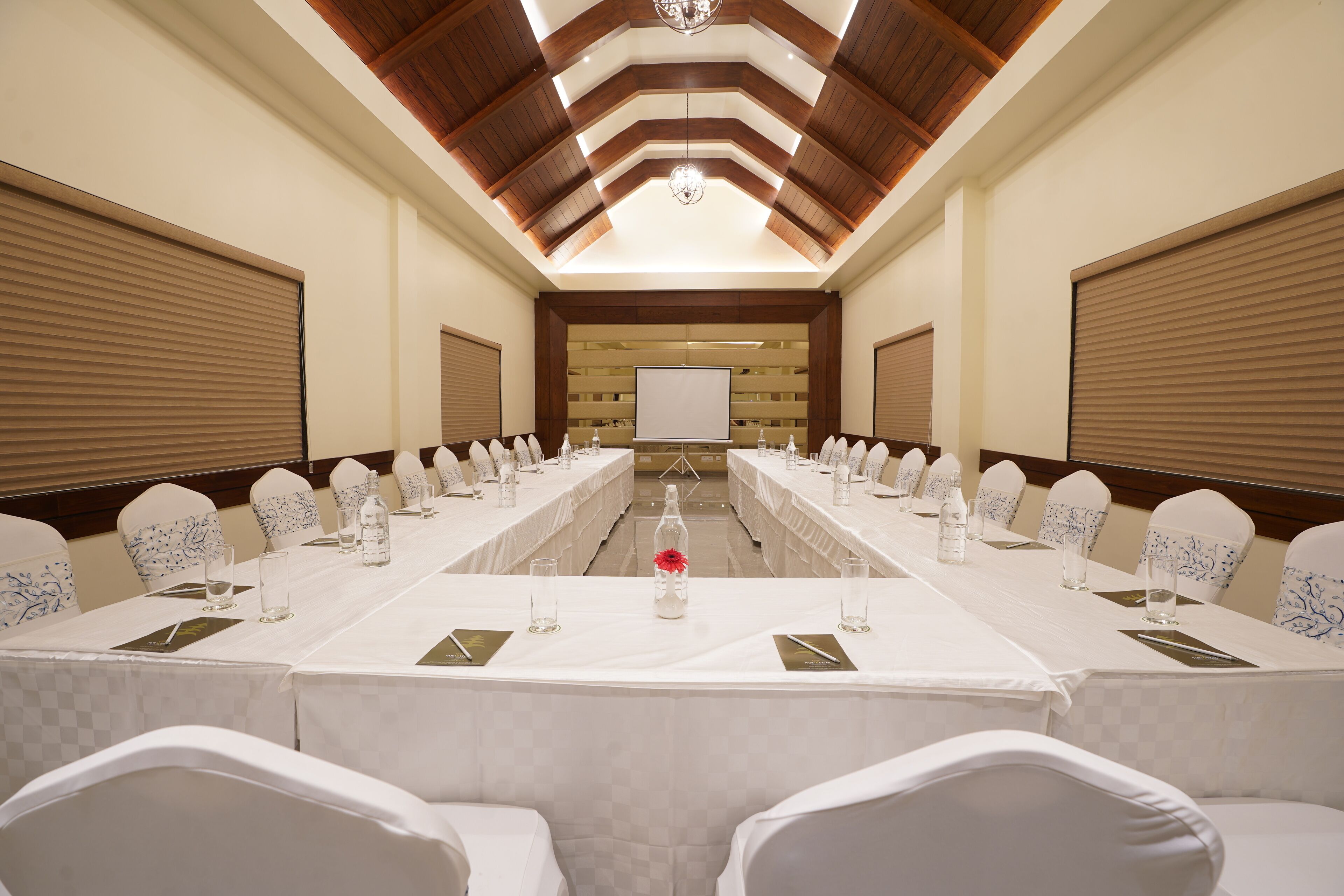 A conference room with a long table, white chairs, and a projector screen at the front.