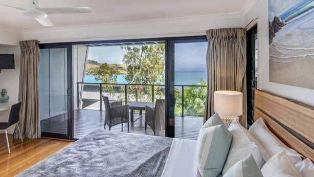 A bedroom with a large bed, a balcony with a table and chairs, and a view of the sea. - Shorelines 12 (Hamilton Island)