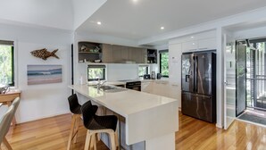 A modern kitchen with a central island, wooden flooring, and a view of the outdoors. - Shorelines 12 (Hamilton Island)