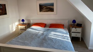 A bedroom with a bed, two nightstands, a desk, a chair, and a painting on the wall. - Vacation home in quiet, relaxing surroundings Zingst / Müggenburg (Zingst)