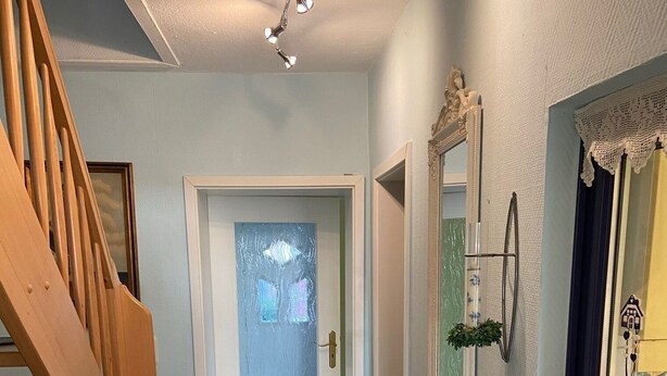 A hallway with a wooden staircase, a white door with frosted glass, a mirror, and a shelf with decorative items. - Vacation home in quiet, relaxing surroundings Zingst / Müggenburg (Zingst)