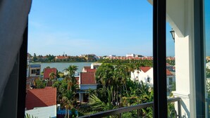 Une vue depuis un balcon donnant sur une zone côtière, avec des bâtiments, des palmiers et une étendue d’eau.