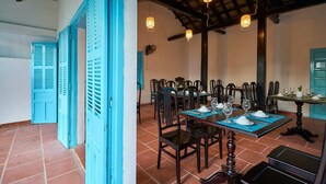 Un espace repas avec des tables et des chaises en bois, des volets bleus et des lanternes suspendues.