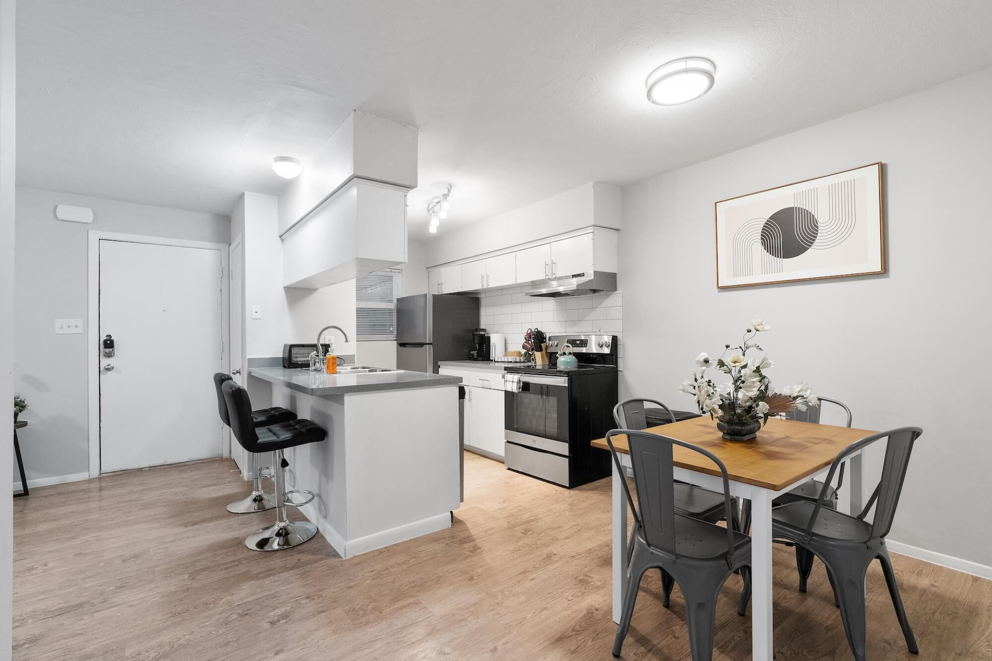 A modern kitchen with a central island, a dining area with a wooden table and metal chairs, and a kitchen counter with appliances.