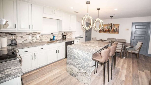 A modern kitchen with white cabinets, a marble island, and a dining area with wooden chairs.
