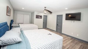 A bedroom with two beds, a ceiling fan, a TV, and a door.