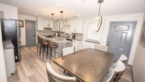 A modern kitchen with white cabinets, a marble island, and a dining area with a wooden table and chairs.