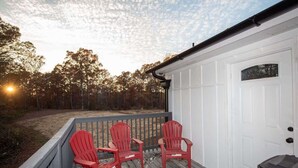 A wooden deck with two red Adirondack chairs, a white garage door, and a view of trees under a partly cloudy sky.