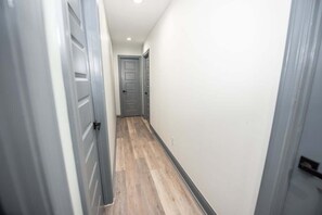 A narrow hallway with wooden flooring and grey doors.