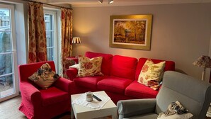 Un salon avec un canapé rouge, un fauteuil gris, une petite table blanche et un tableau accroché au mur.