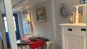 Un coin repas avec une table et des chaises, une horloge au mur et un meuble sur lequel est posé un objet décoratif.