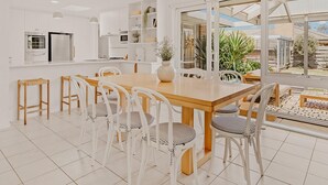 Een moderne keuken met witte kasten, een houten eettafel en witte stoelen. Er is een groot raam met uitzicht op de achtertuin.