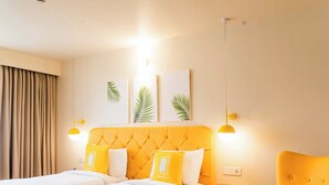 A hotel room with two beds, a yellow armchair, a small round table, and a nightstand. - Bloom Hotel - Jammu (Jammu)