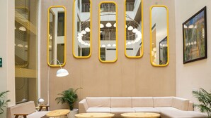 A modern lounge area with a beige sofa, yellow ottomans, and a patterned floor. - Bloom Hotel - Jammu (Jammu)