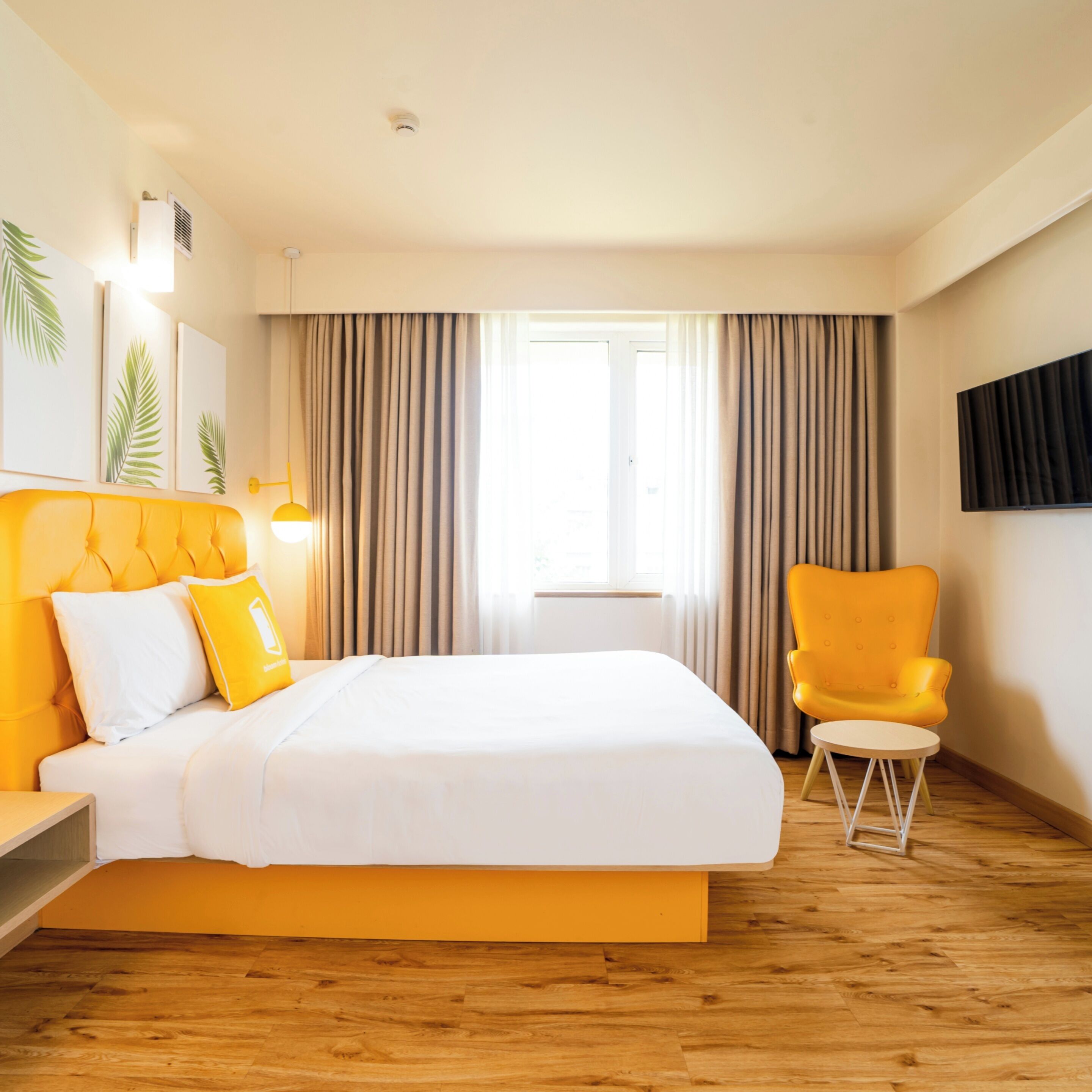 Habitación de hotel con una cama grande, una mesita pequeña, una silla y un televisor montado en la pared.
