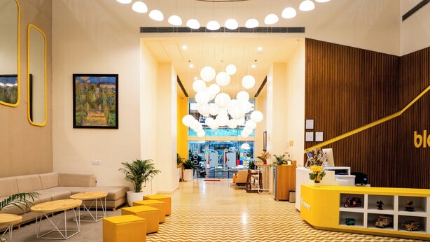 A modern hotel lobby with a central chandelier, seating area, reception desk, and a view into the restaurant. - Bloom Hotel - Jammu (Jammu)