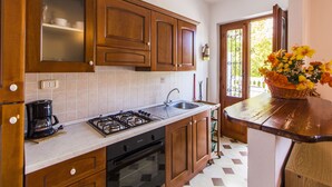 A kitchen with wooden cabinets, a gas stove, a coffee maker, and a sink. - Studio in Residence near the sea in a beautiful park (Campiglia Marittima)