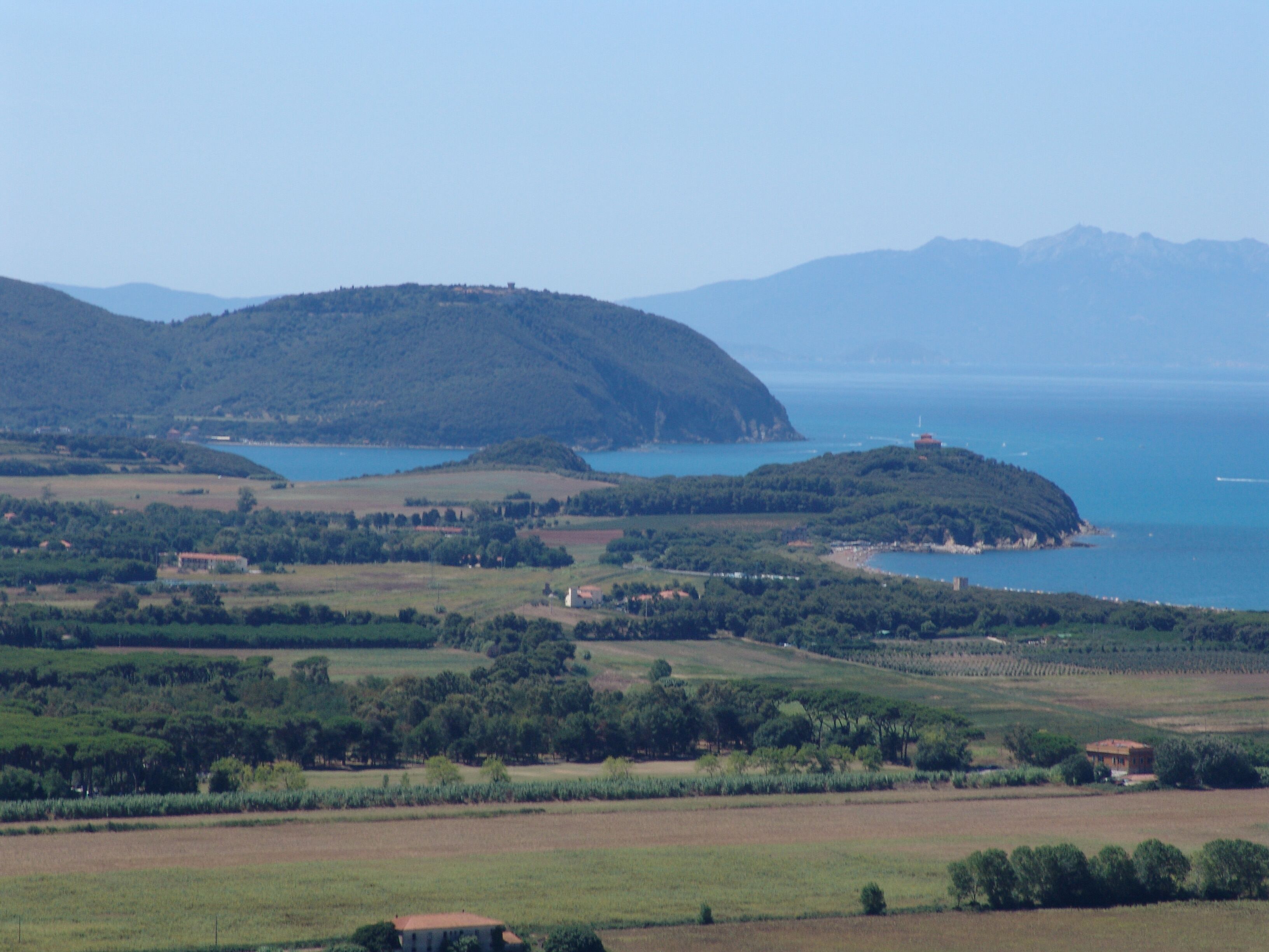A coastal landscape with rolling hills, a body of water, and scattered buildings.
