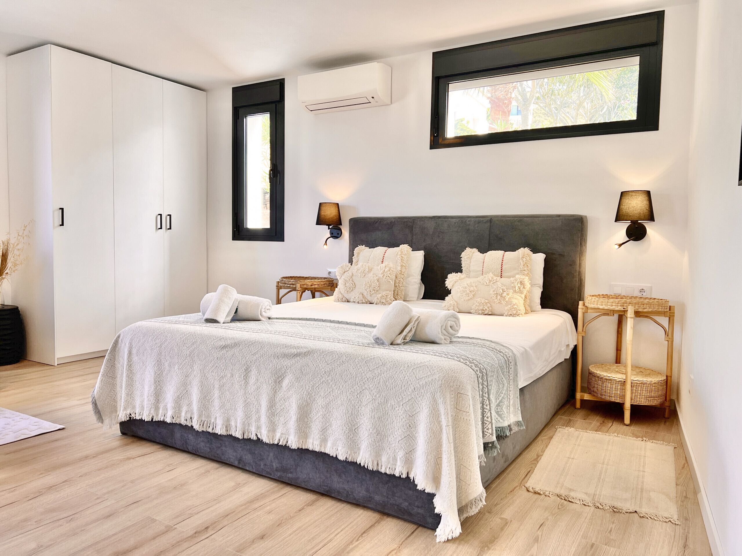 A modern bedroom with a large bed, two bedside tables, a wardrobe, and a window with a view.