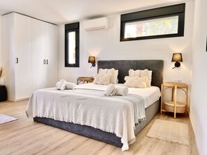 Un dormitorio moderno con una cama grande, dos mesitas de noche, un armario y una ventana con vistas.