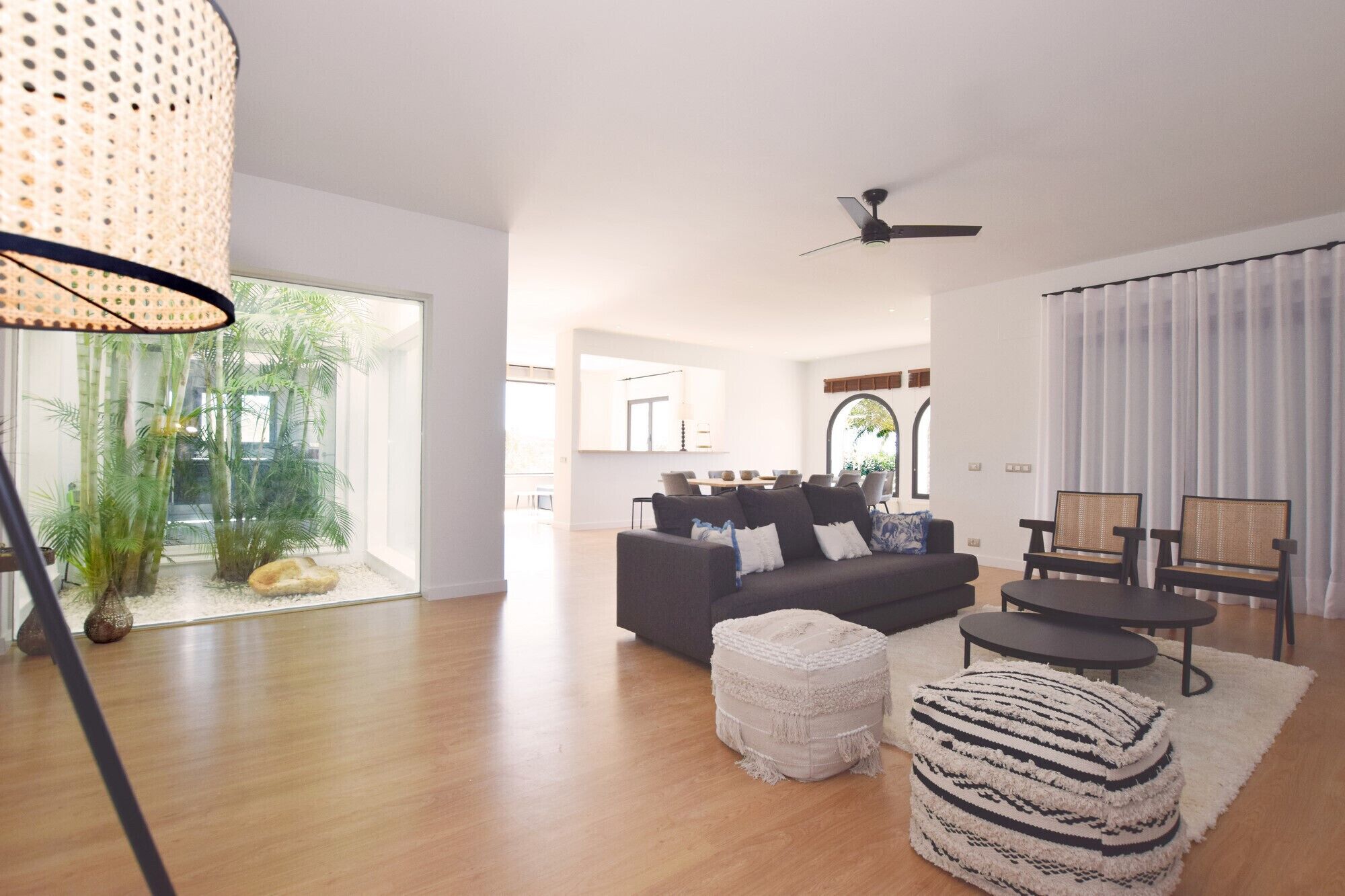 A spacious living room with a dark sofa, ottomans, and a dining area in the background.