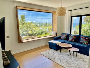A modern living room with a large window, a blue sofa, a small round table, and a TV on a black stand. - Comfortable villa in Cala de los Alemanes, Mediterranean style. (Tarifa)