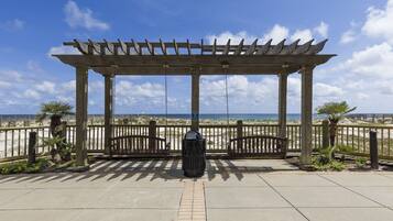 A wooden pergola with a view of the beach, a trash can, and a paved walkway.