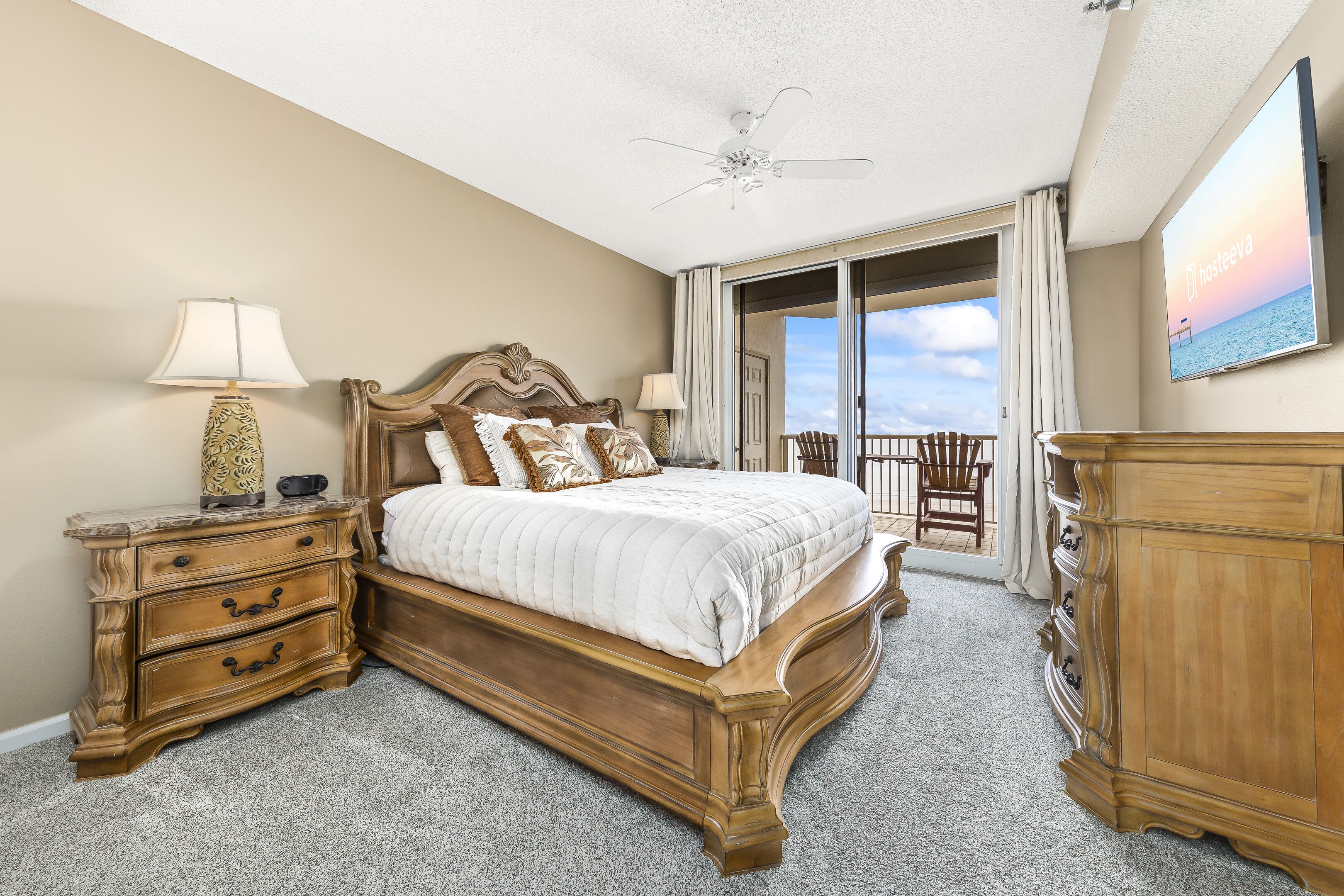 A bedroom with a large bed, a nightstand with a lamp, a dresser, and a TV on the wall.