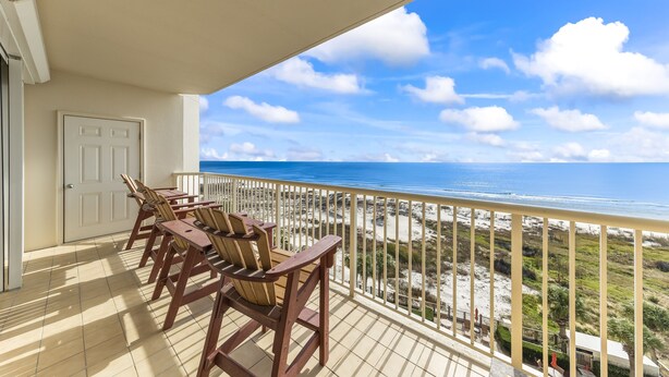 En balkon med træstole og udsigt til stranden og havet.