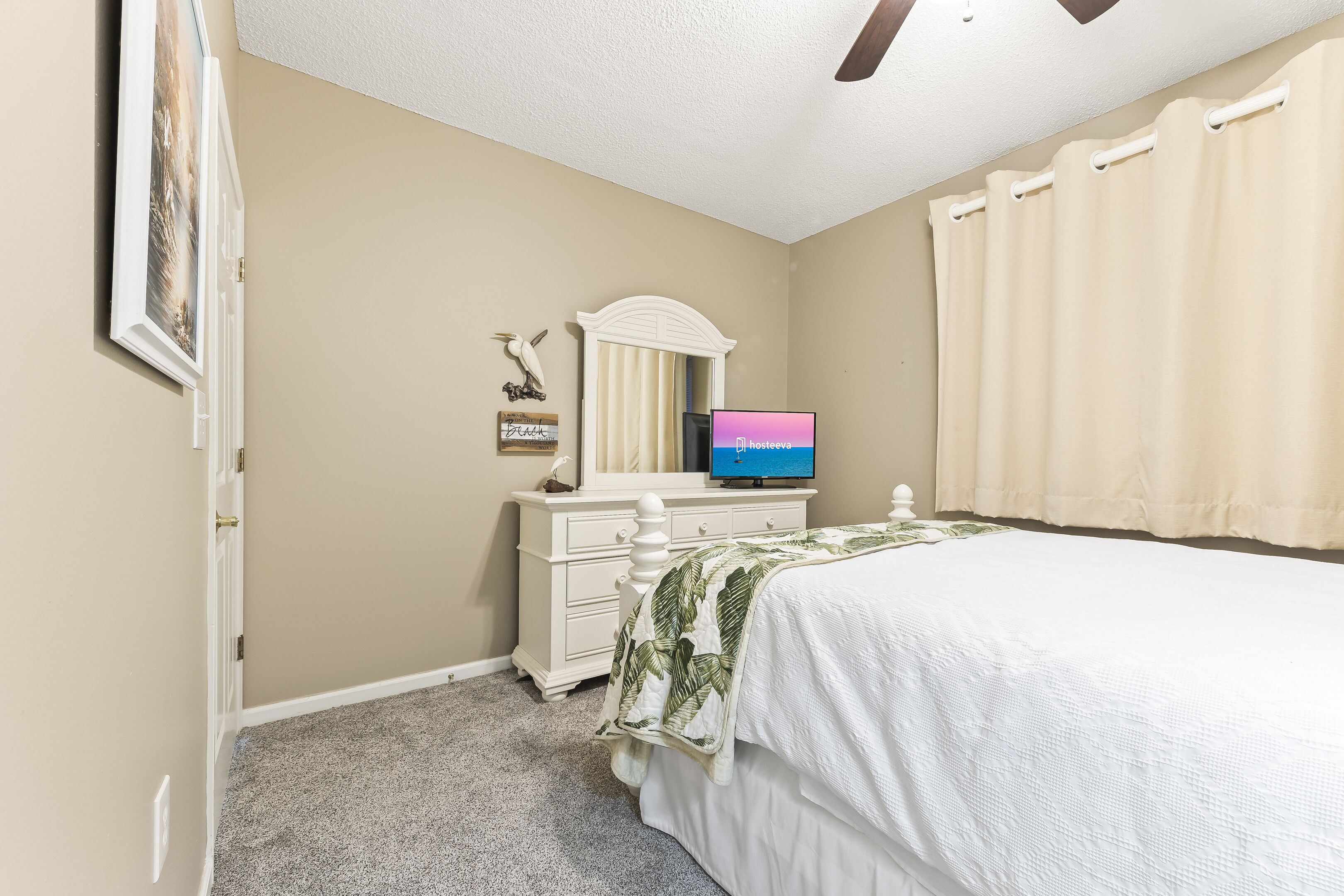 A bedroom with a bed, a dresser, a television, and a ceiling fan.