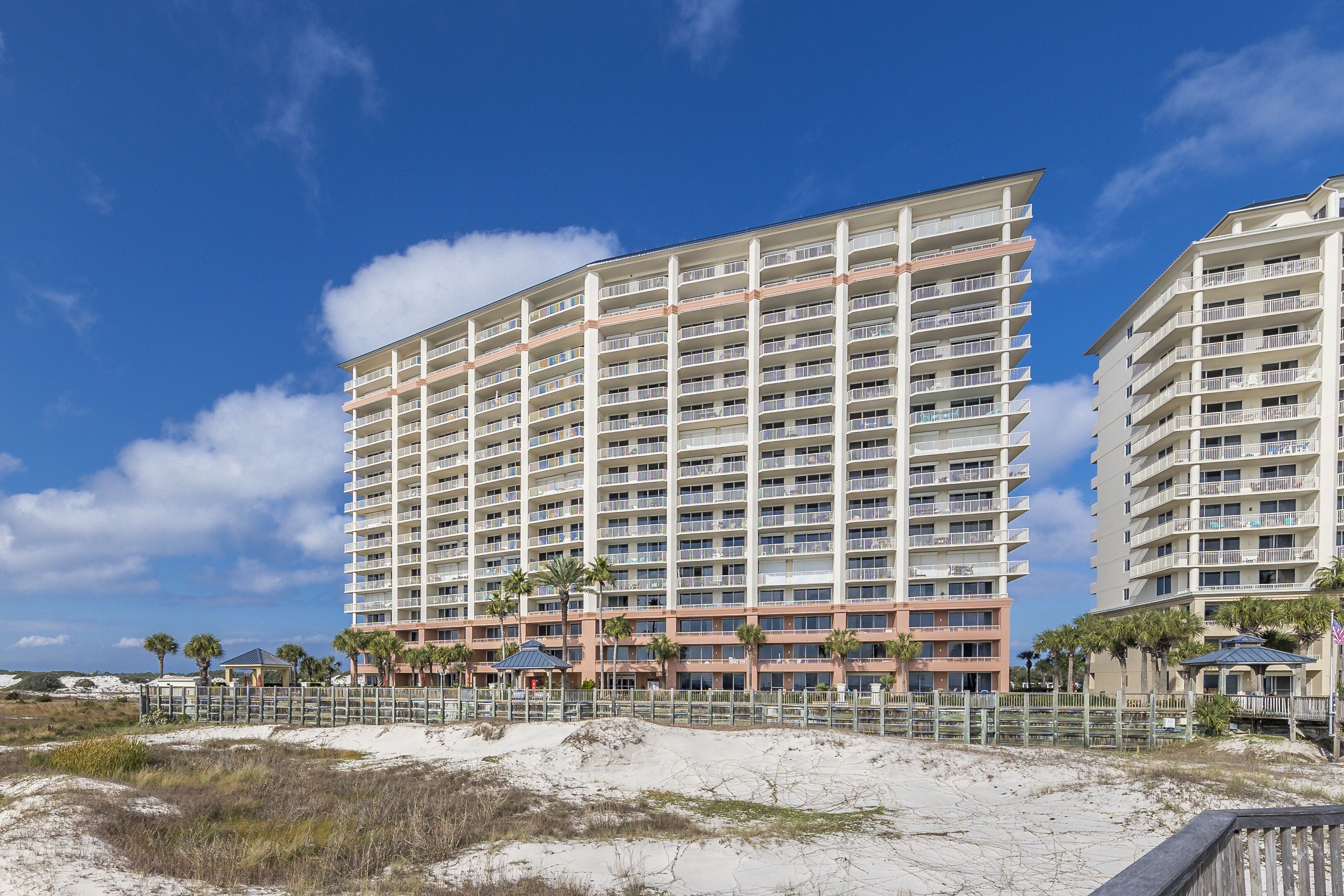 A multi-story hotel with balconies, located near a sandy beach.