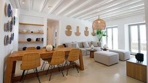 Een moderne woonruimte met een houten eettafel, rieten stoelen, een grijze bank en een groot raam dat voor natuurlijk licht zorgt.