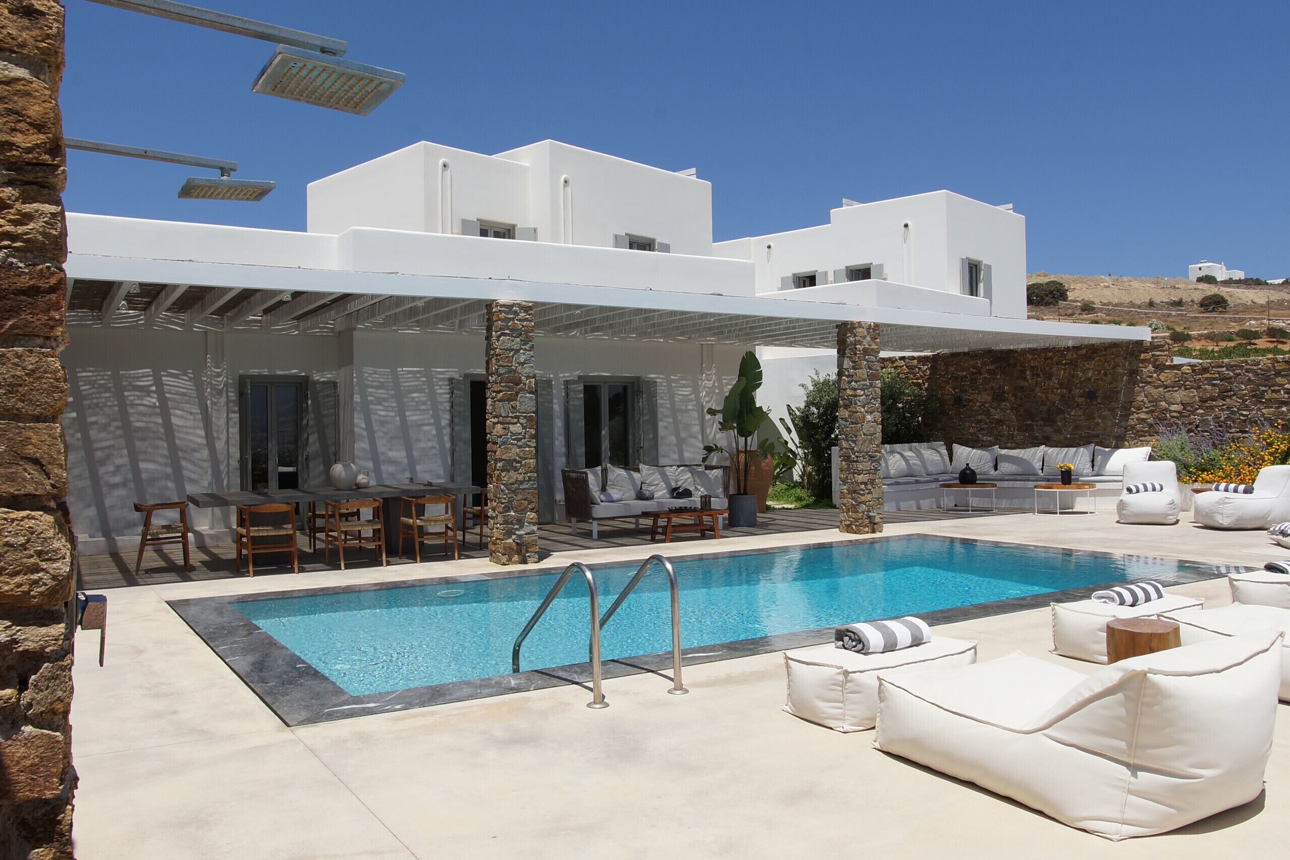 A modern poolside area with a clear blue pool, stone pillars, and white outdoor furniture.