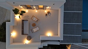 Een terras op het dak met een minimalistisch ontwerp, met een witte zithoek, een potplant en een kleine tafel.