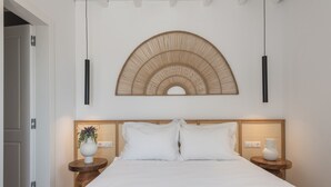 Een slaapkamer met een groot bed, twee nachtkastjes met lampen, een decoratief kunstwerk boven het bed, en een deur aan de linkerkant.