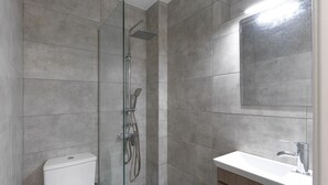 Un bany modern amb dutxa de vidre, vàter i un lavabo amb mirall a sobre.
