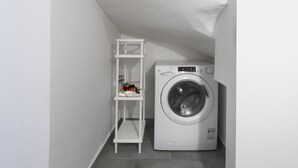 Una bugaderia petita amb una rentadora i un moble estant blanc.